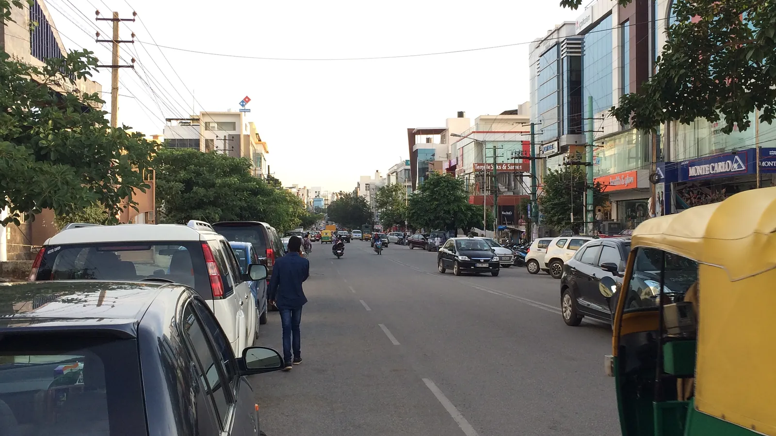 A residential street in HSR Layout, Bengaluru, with parked cars and an auto-rickshaw