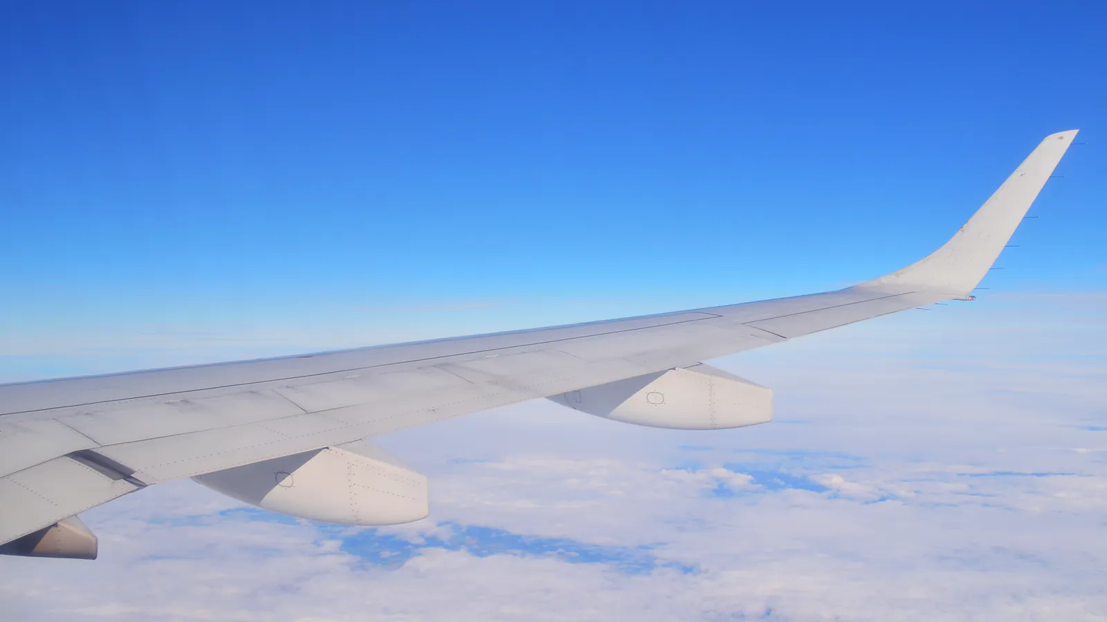 An aircraft wing over a carpet of white clouds in a blue sky