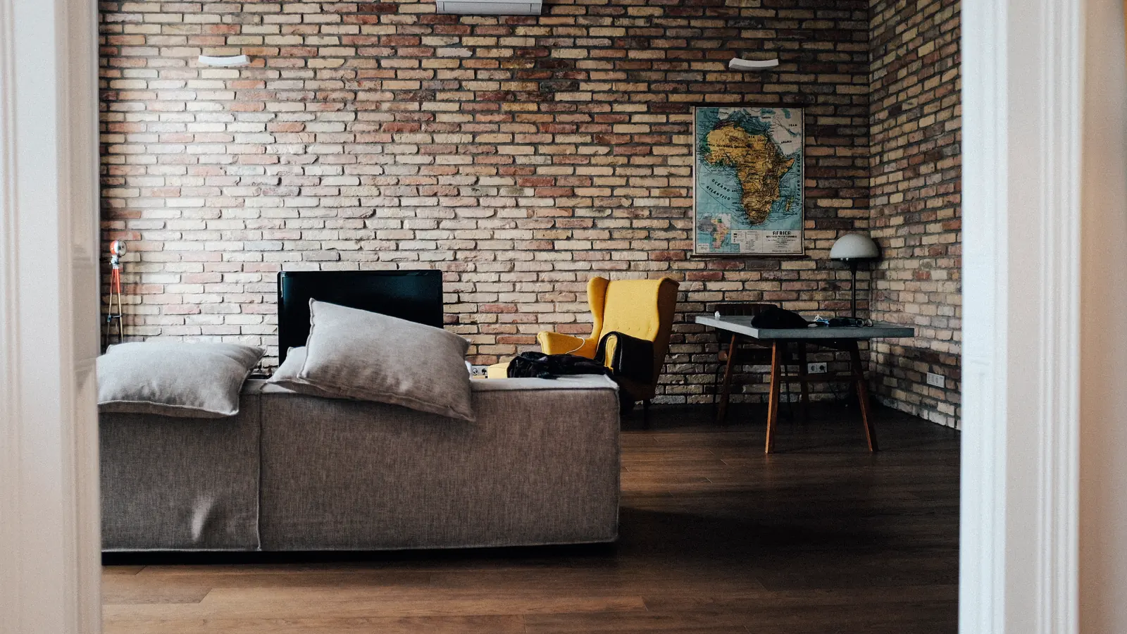 A furnished apartment living room with a grey sofa against an exposed brick wall