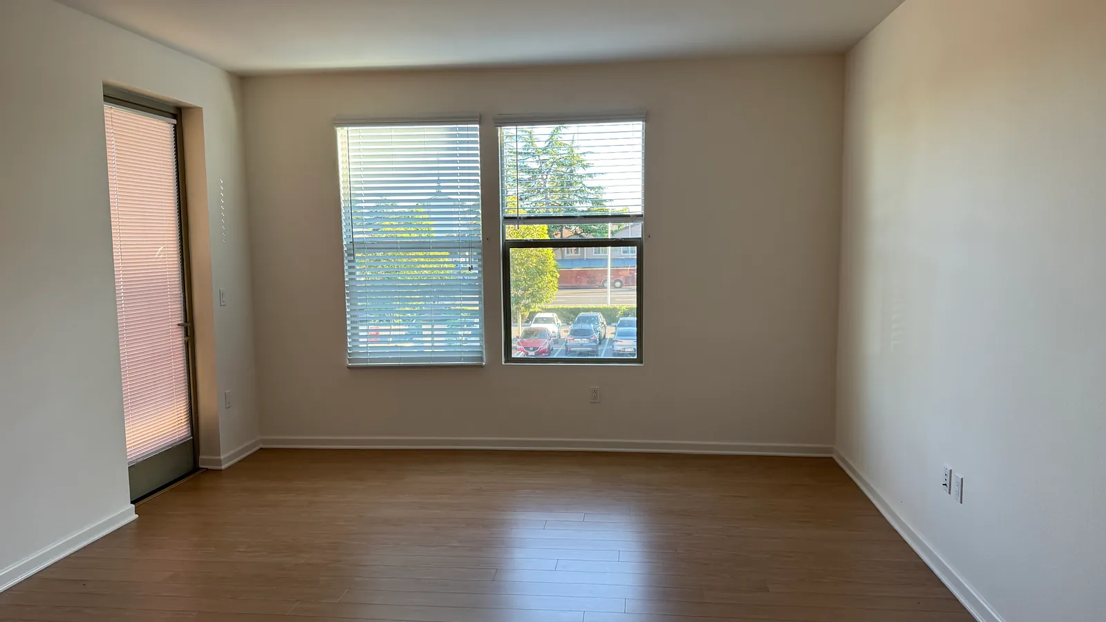 An empty, freshly painted apartment room with a window and wooden flooring